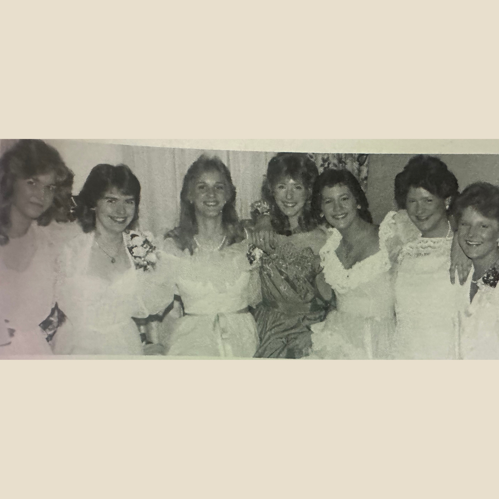 Group of 7 teenage girls smiling in a photo at prom