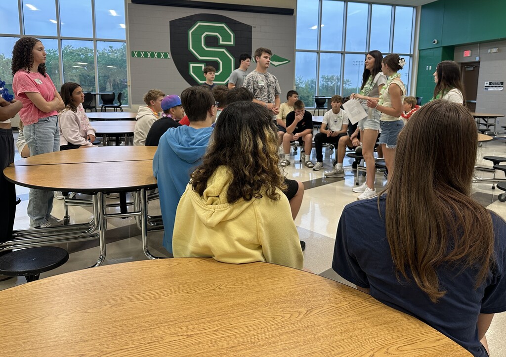 High School students speak to 8th graders sitting at the cafeteria tables.