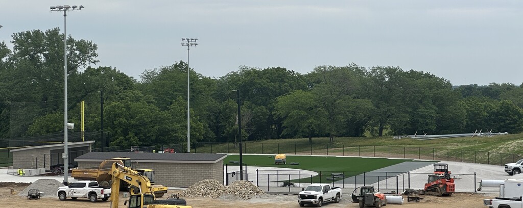 Construction equipment is parked around the softball field as turf is starting to be laid.