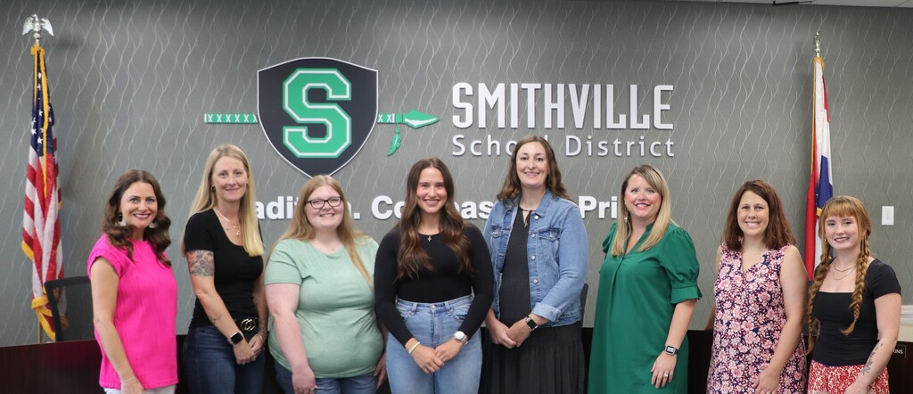 Nine new employees pose for a picture in front of the Smithville School District logo
