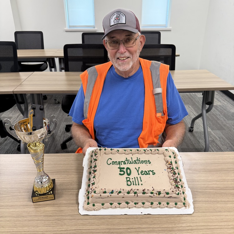 Bill holds a cake that says 50 years and a trophy.