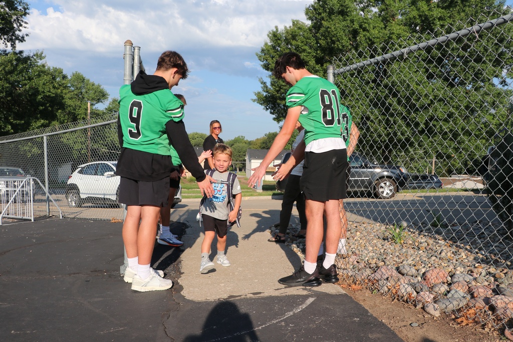 football players greet elementary student when they arrive at school