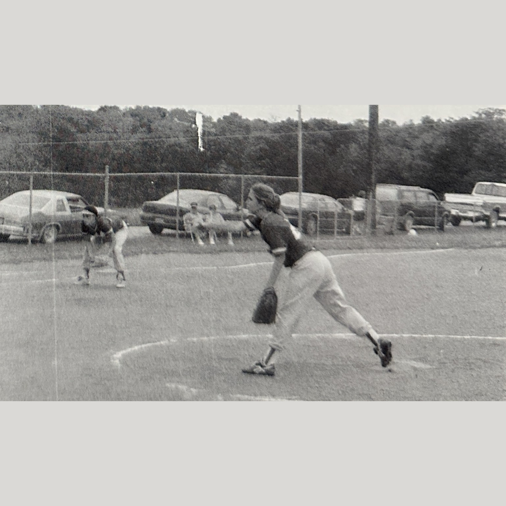 in a classic picture a softball player pitches the ball while third base is down and ready.