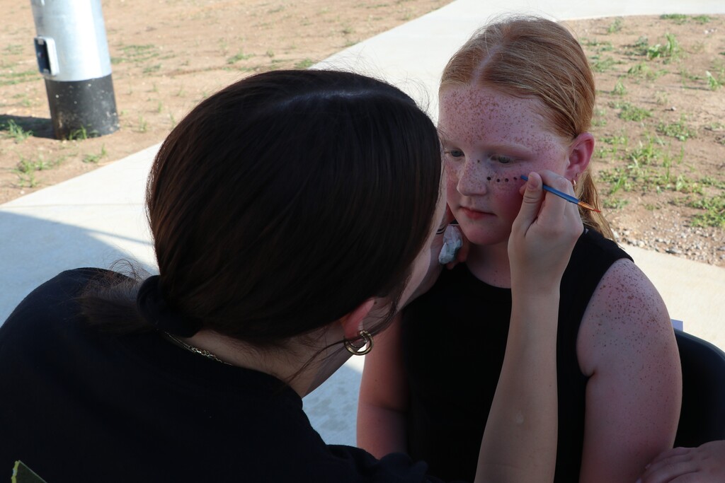 a little girl getting black dots painted on her face