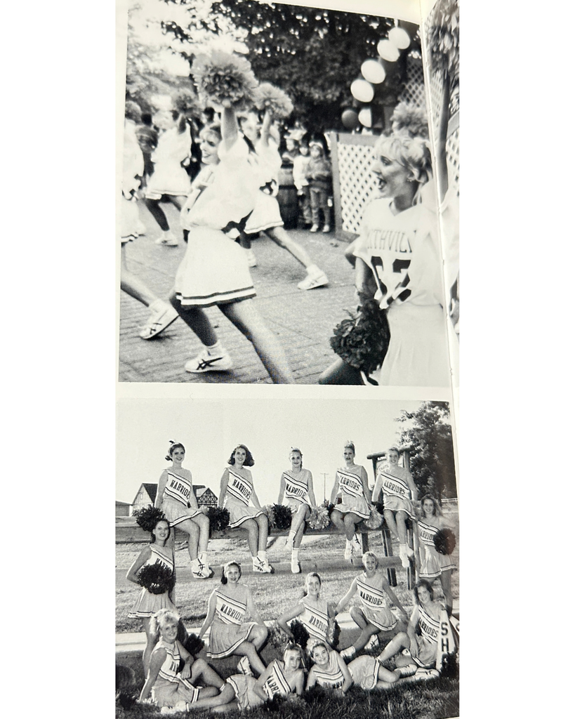 a black and white photo of cheerleaders sitting with their poms and some sitting on a bench, others sitting or laying on the ground. They have uniforms on that say "WARRIORS"