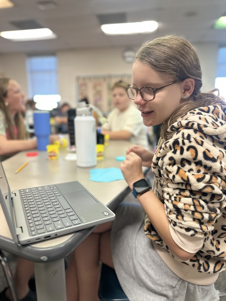 A girl looks at her computer to find the shape of the next cuneiform letter in her name