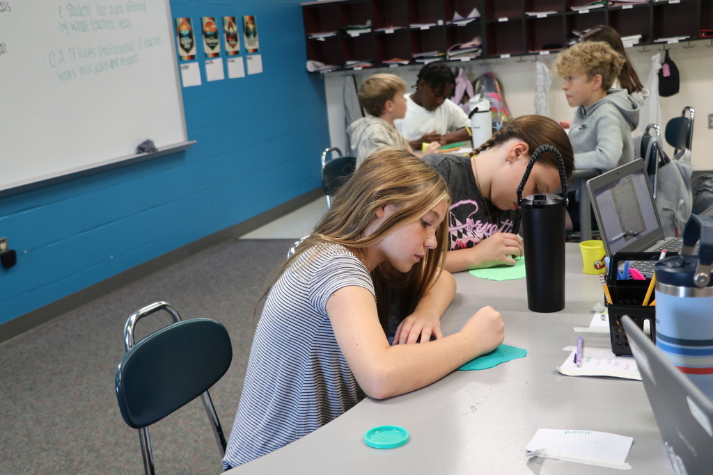 A girl carves her name into teal playdough using cuneiform