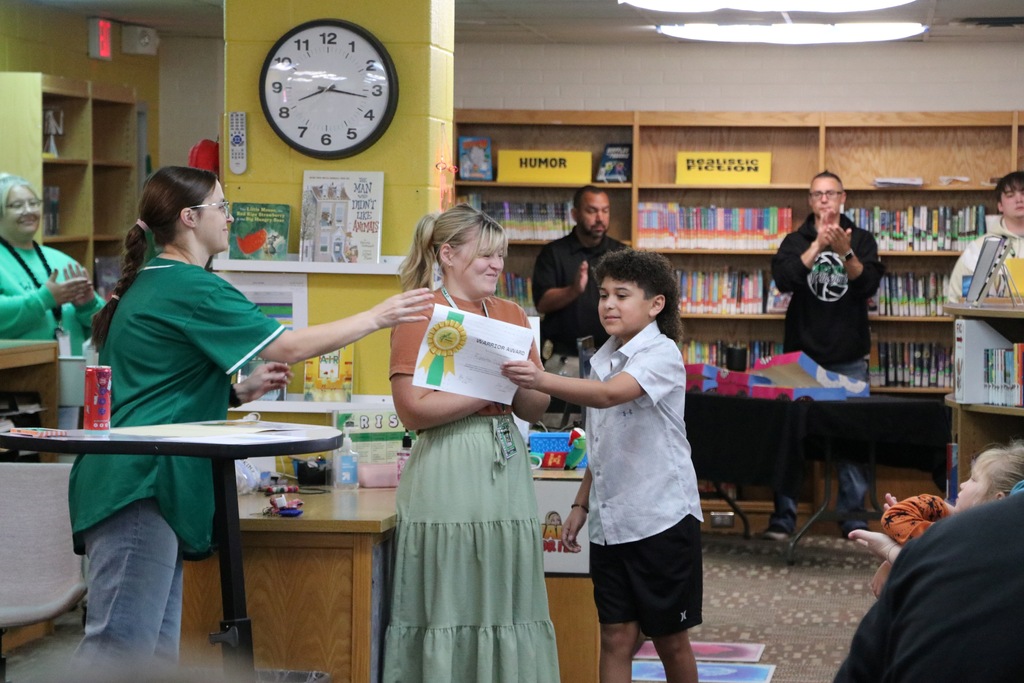 A boy receives a certificate from the principal while the teacher claps.