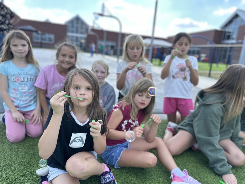 Girls sit on the new turf and blow bubbles