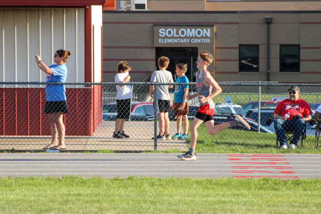 student running on track with solomon elementary in back