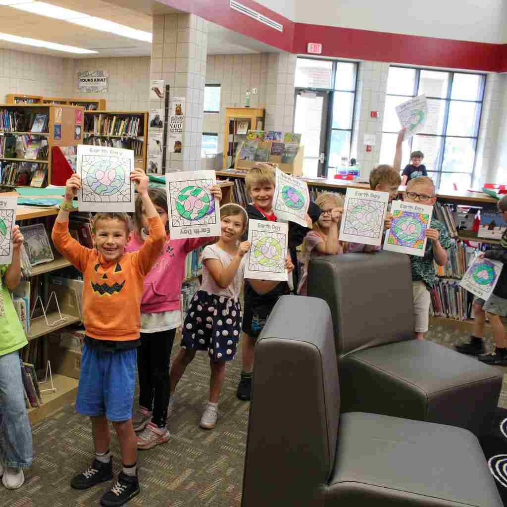 group of students excitedly holding up their artwork of a color by number of the Earth