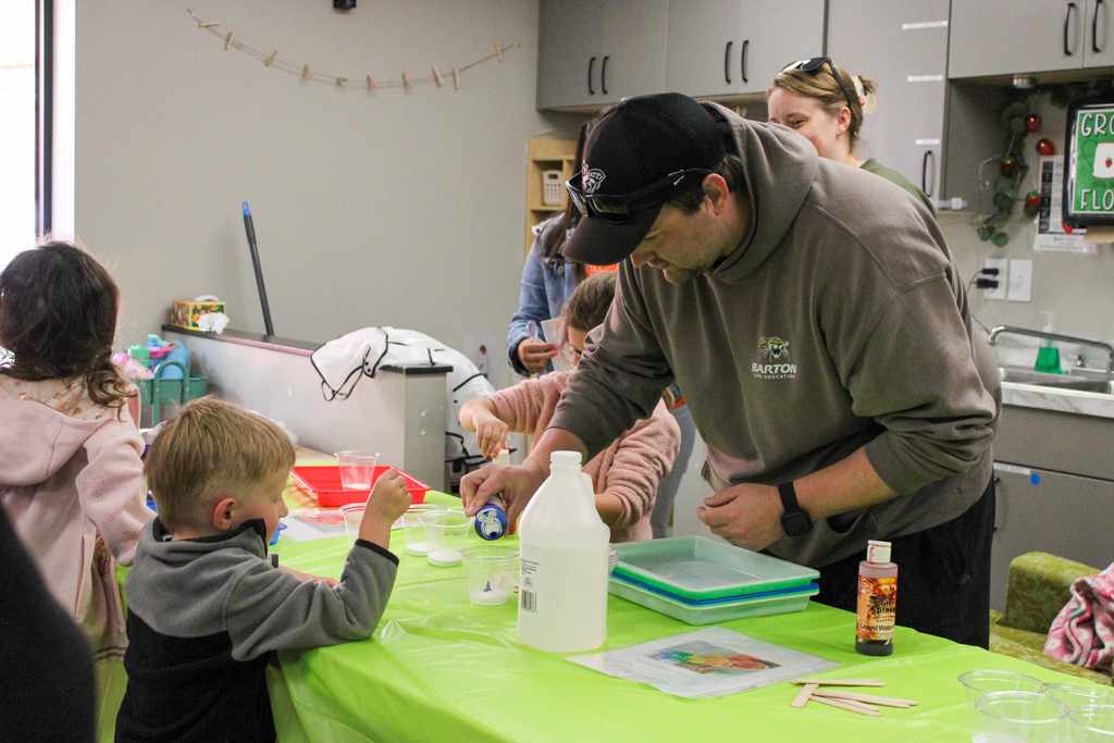 A group of students gathered around a table, focused on a collaborative hands-on project with their teacher.