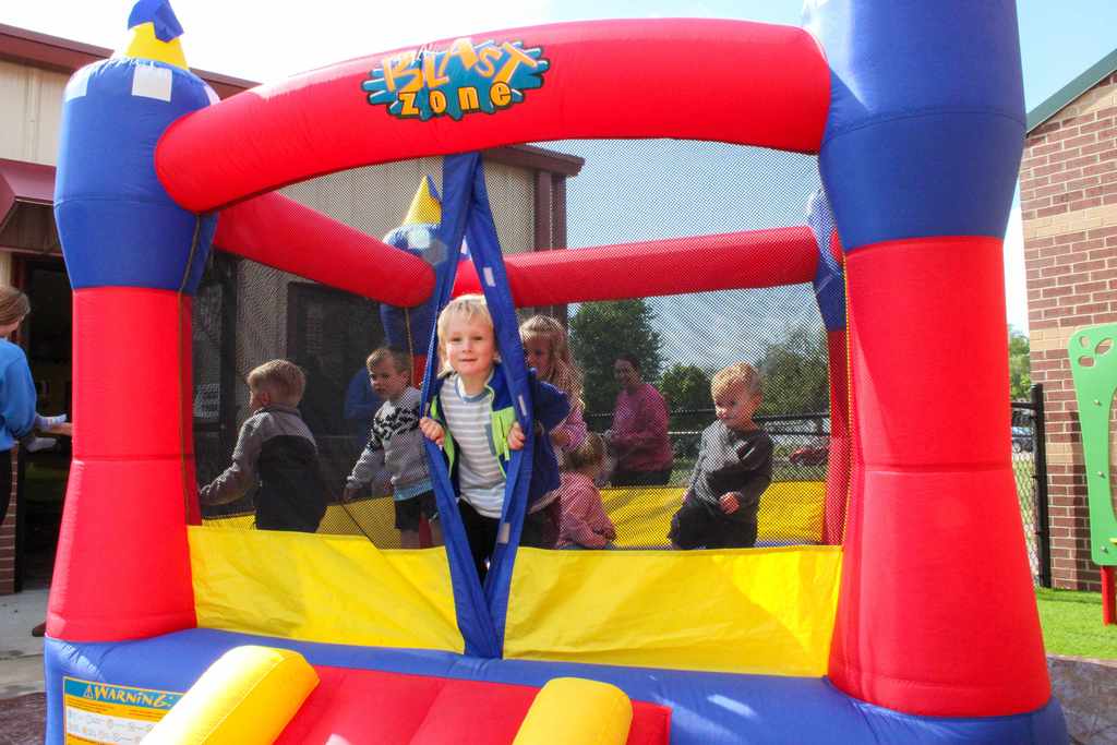 A young student smiling while sitting inside a red inflatable structure, enjoying a physical education or play session.