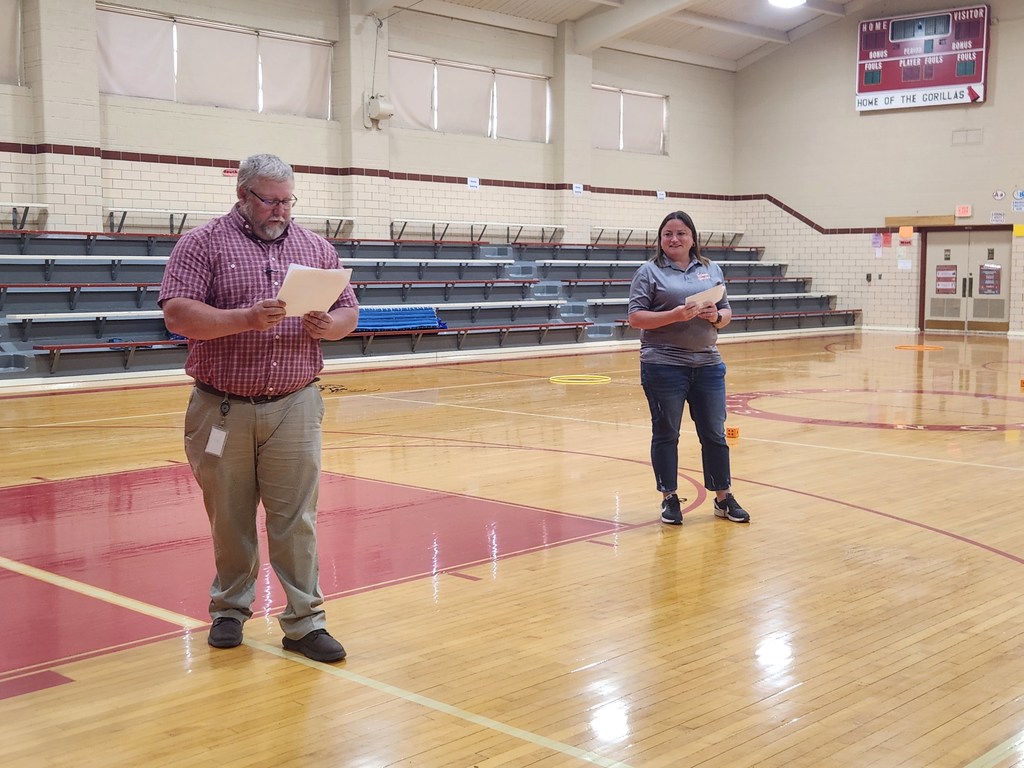 two adults standing in a gymnasium reading off a script