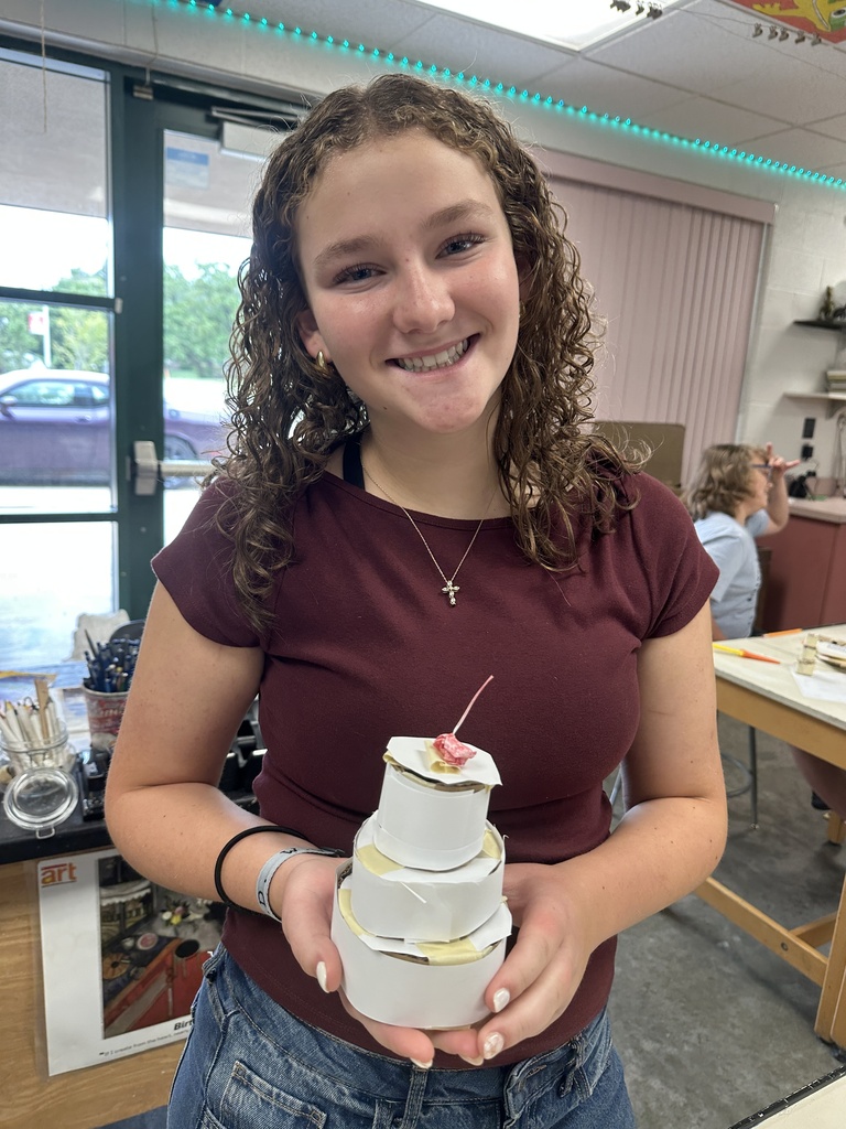 student showing off their handmade 3 tier cake madee out of cardboard