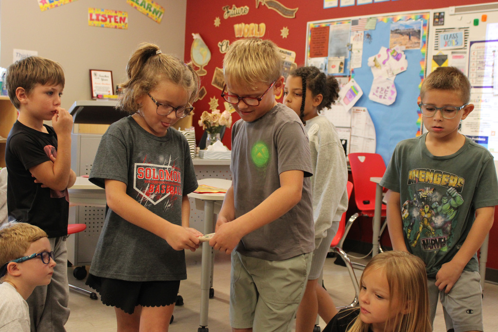 pair of students working together to place their boat in the water with peers watching on