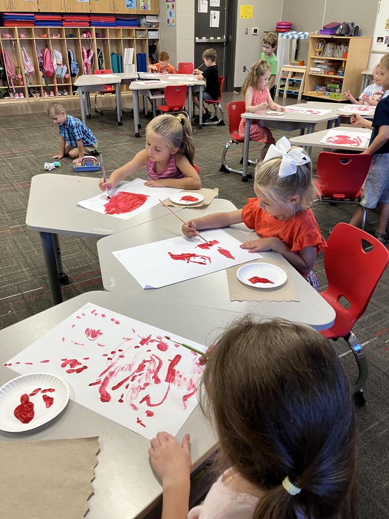 students painting with red paint on white paper
