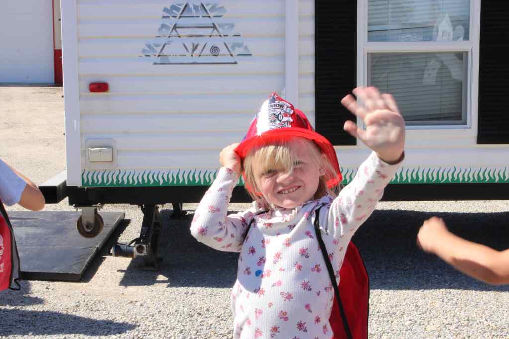 student waving excitedly while holding onto their fire safety hat