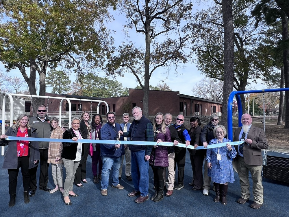 group of people standing on playground about to cut a ribbon with large scissors