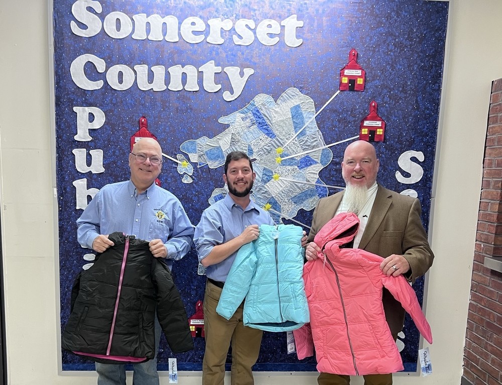 three men holding coats while smiling in front of a large map of Somerset County