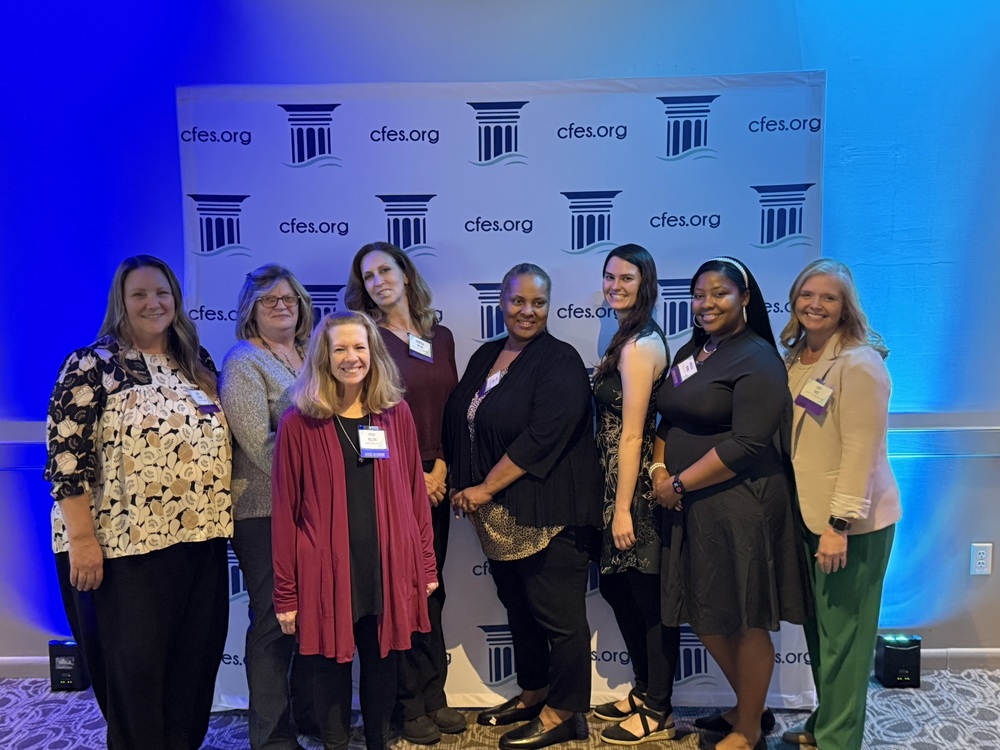 eight women in front of a backdrop that has "cfes.org" and a column image on it