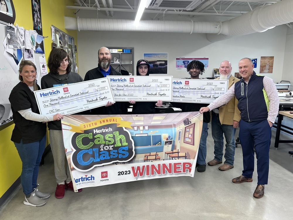 people standing in a room holding a banner and three big checks