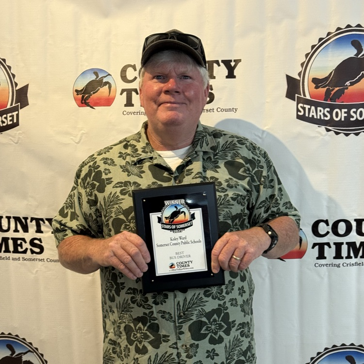 Man in front of a backdrop, holding a plaque and smiling