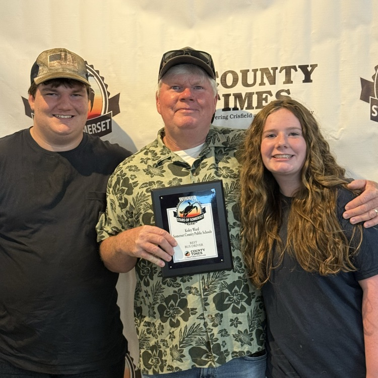 three people standing in front of a backdrop, and one is holding a plaque
