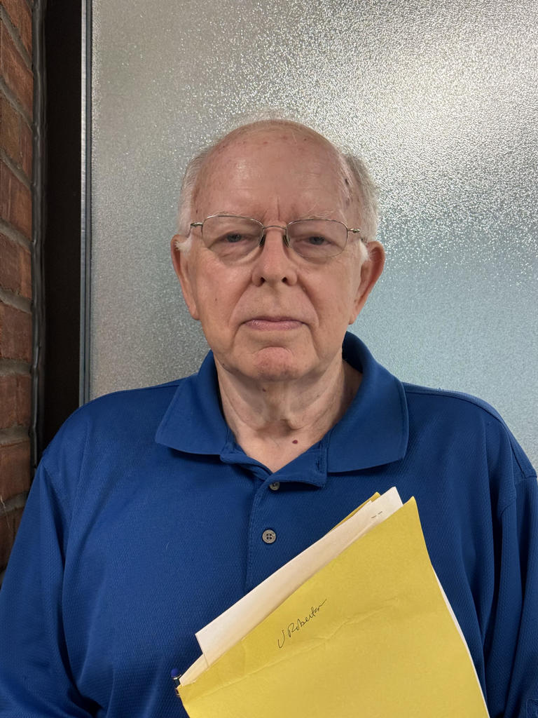 man in blue shirt and glasses with a neutral facial expression