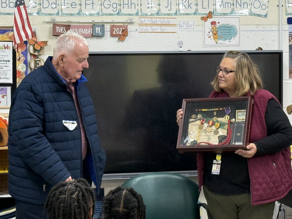 teacher holding a display box of war medals and other military regaliia as an older gentleman looks on