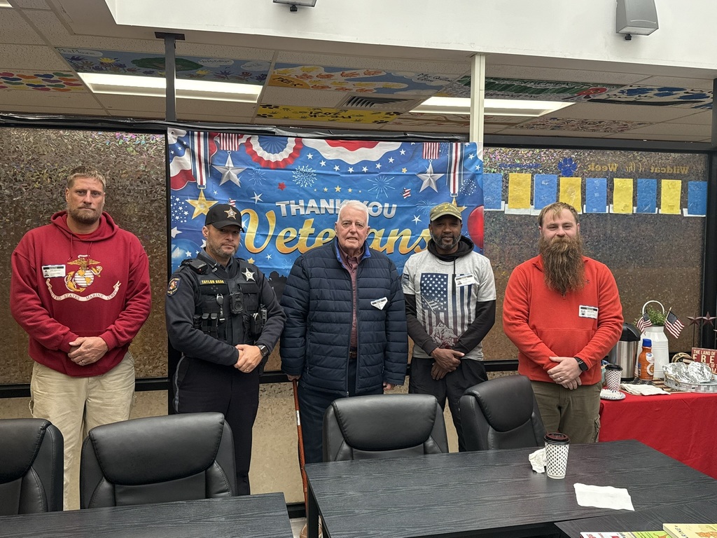 five men standing in front of a "thank you veterans" flag in the background 