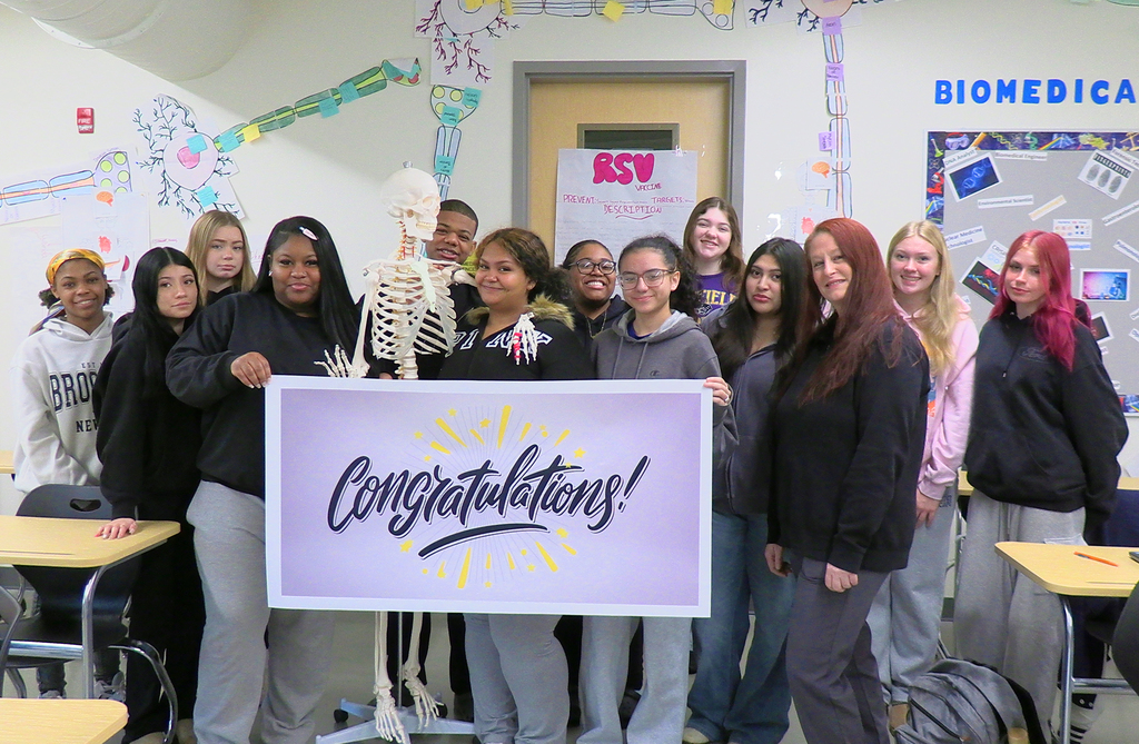 Students in classroom with teacher holding a large sign that says “Congratulations”