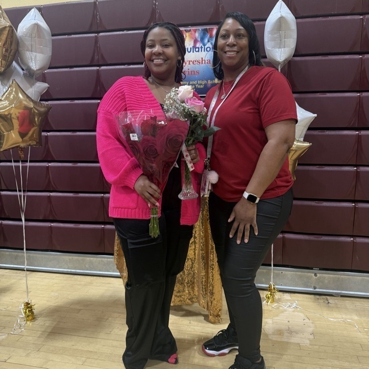 two teachers smiling and holding flowers in a gymnasium