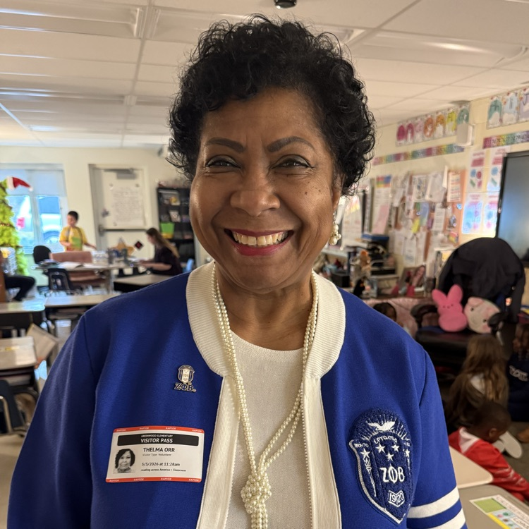 woman in blue sweater reading a book to students in a classroom