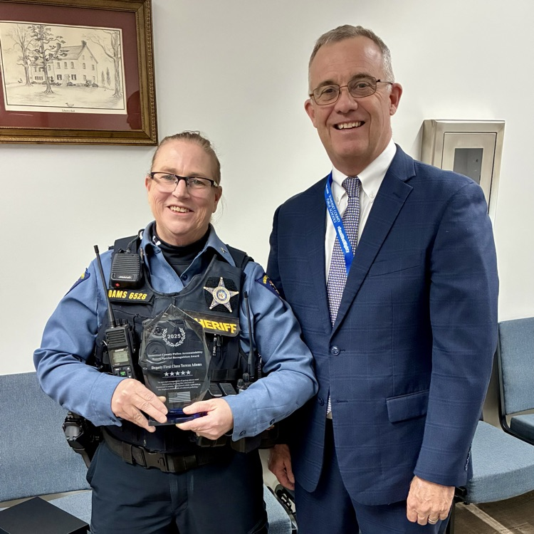 image of female police officer and a man in a suit smiling in a room with white walls and wooden floor