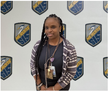 R. Tull smiling standing in front of SIS Herons banner