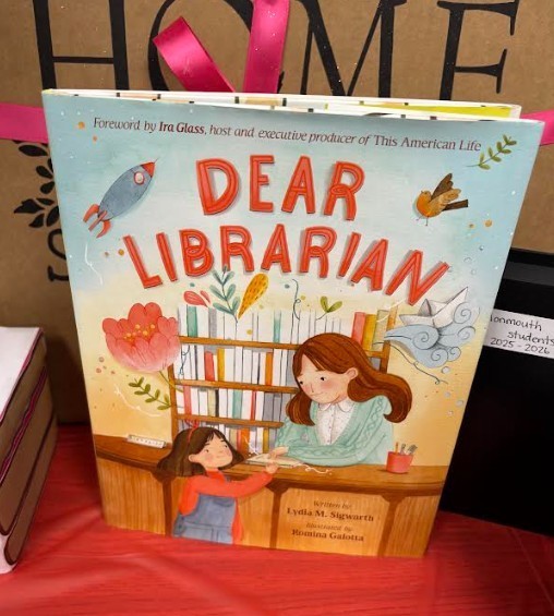 "Dear Librarian" book cover shows a girl and a librarian. Bright colors and illustrations. On a red table.
