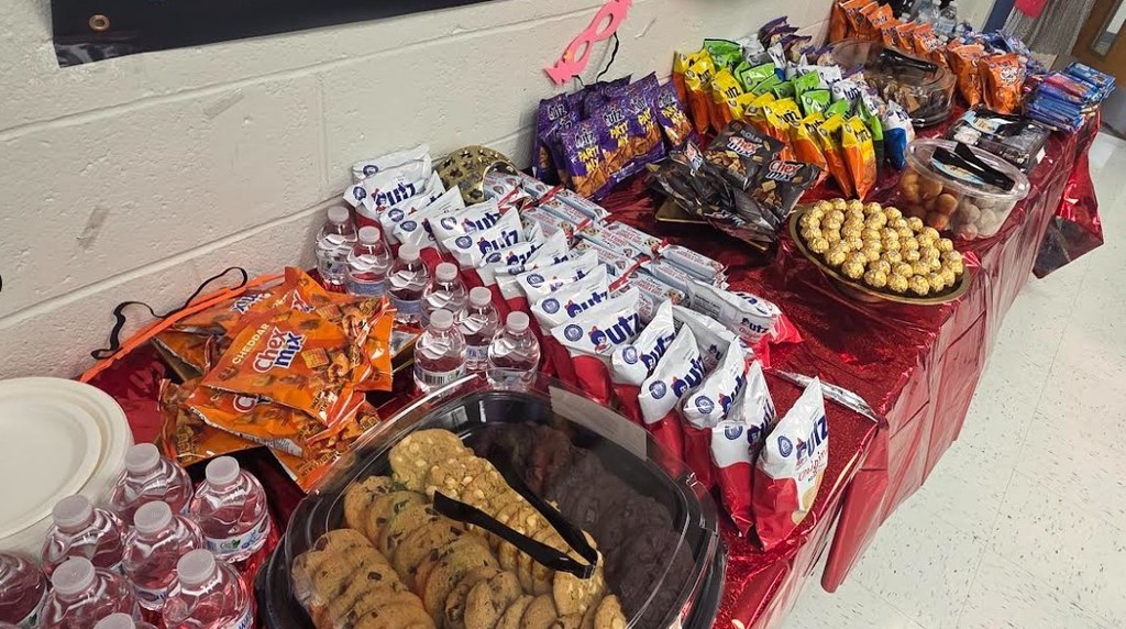 A table covered in red cloth, displaying various snacks, cookies, and drinks on plastic tongs.