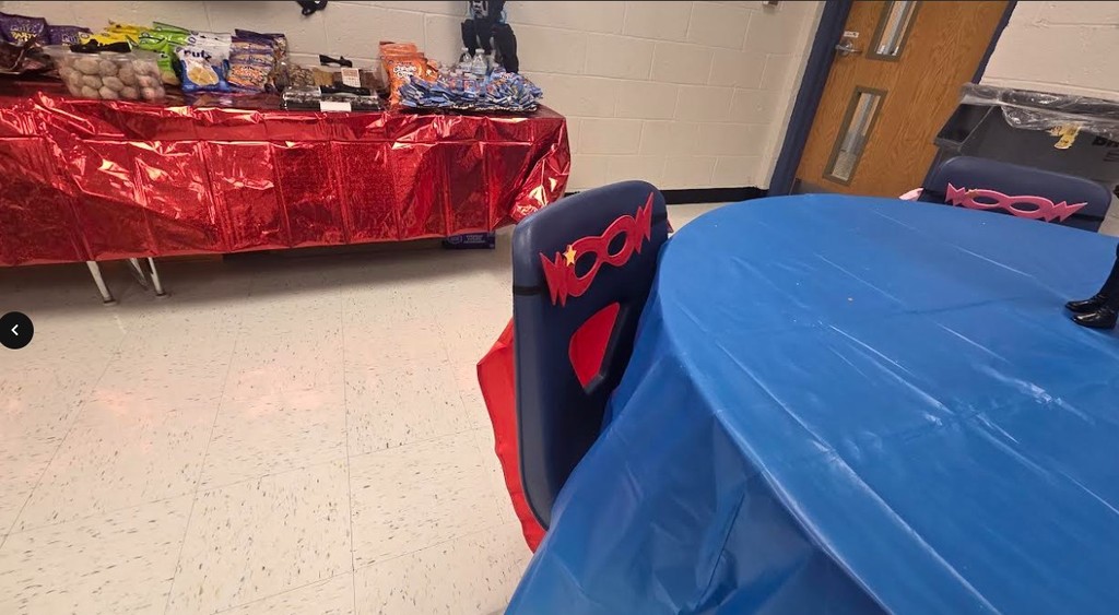 Two tables with red and blue plastic covers. One has snacks, the other a red chair.