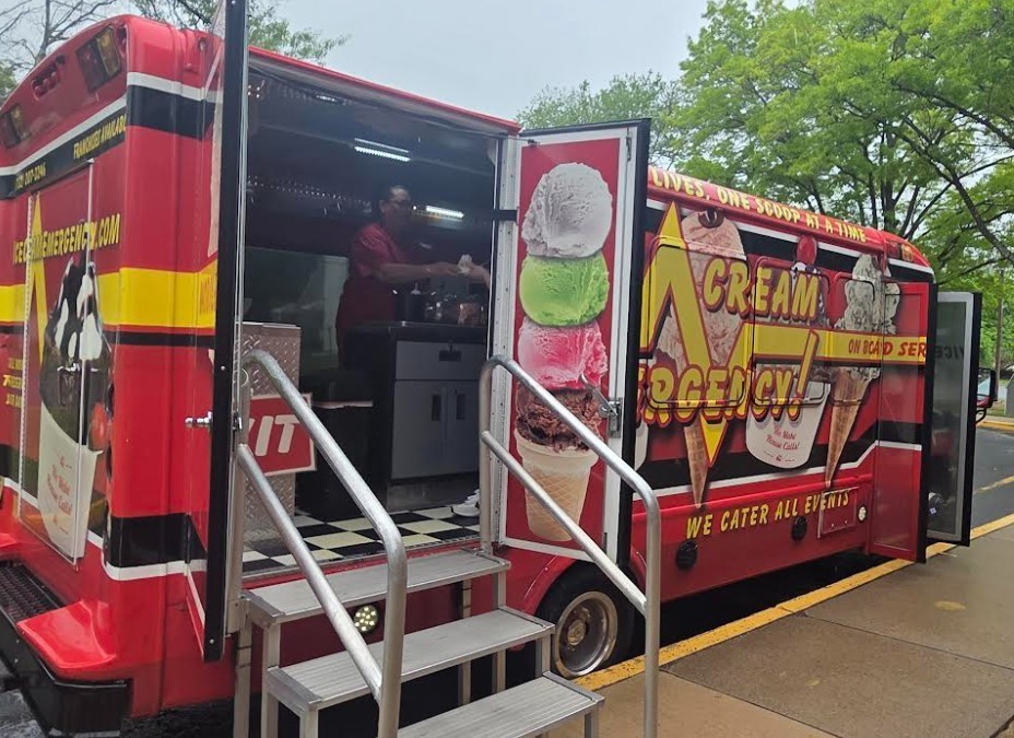 A red ice cream truck with open doors, displaying ice cream images on the side, parked on a curb.