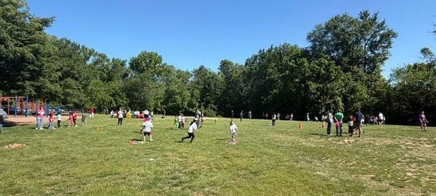 A group of people are outdoors in a grassy field with trees, some standing and some running.