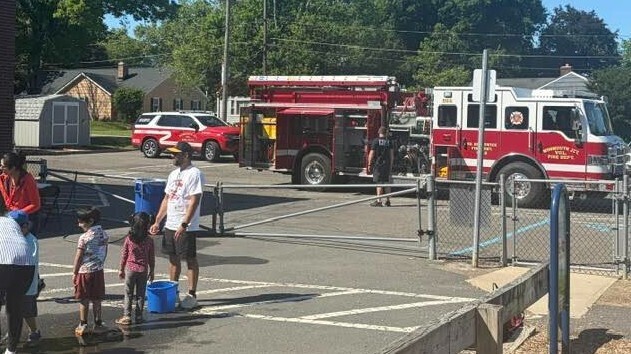 Red fire truck parked with emergency personnel on a street, with people standing nearby.