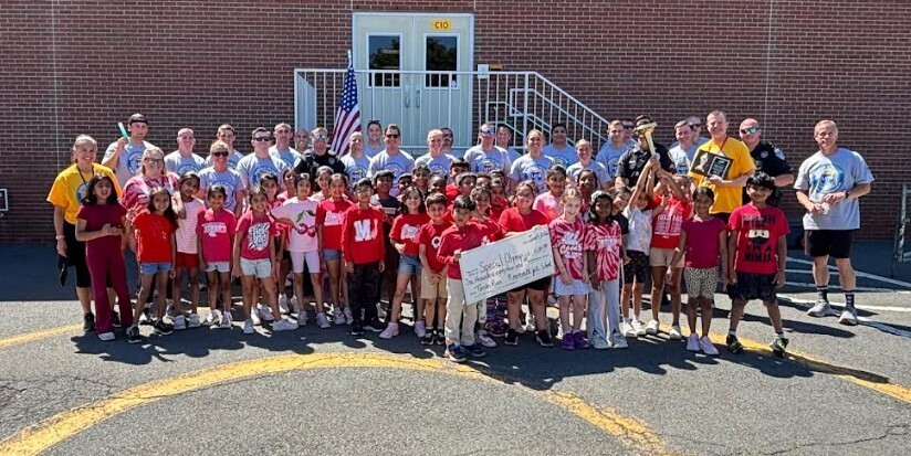 A group of people stands outside a brick building. Some wear red shirts, while others wear white.