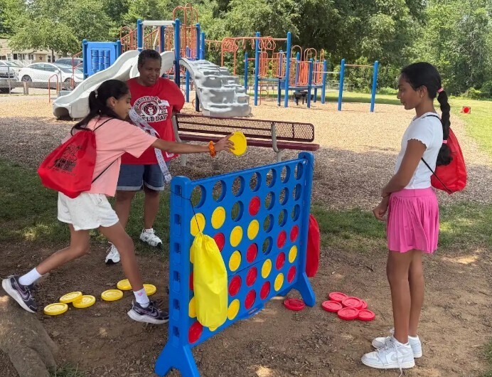 Children playing a game of giant connect four on a playground with a bench and slide in the background.