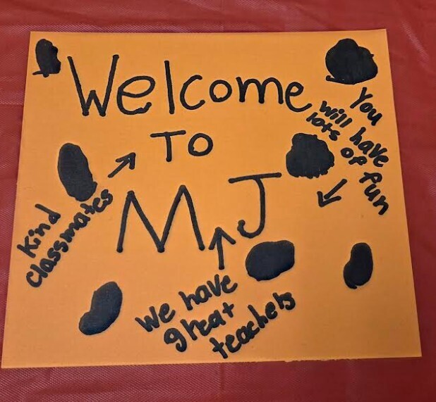 An orange sign with black writing and footprints says "Welcome to MJ." It also mentions kind classmates and great teachers.