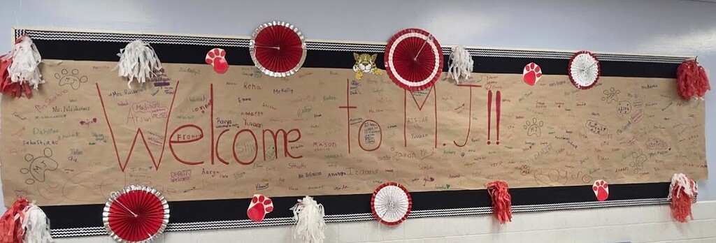 A large sign says "Welcome to MJ" with red and white decorations. A wall with a white background is in the background.
