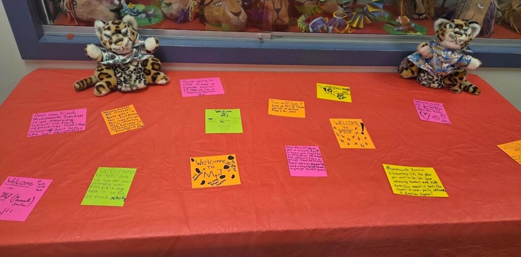 Two stuffed animals on a red table with yellow and pink sticky notes. Behind, a display case with stuffed animals.
