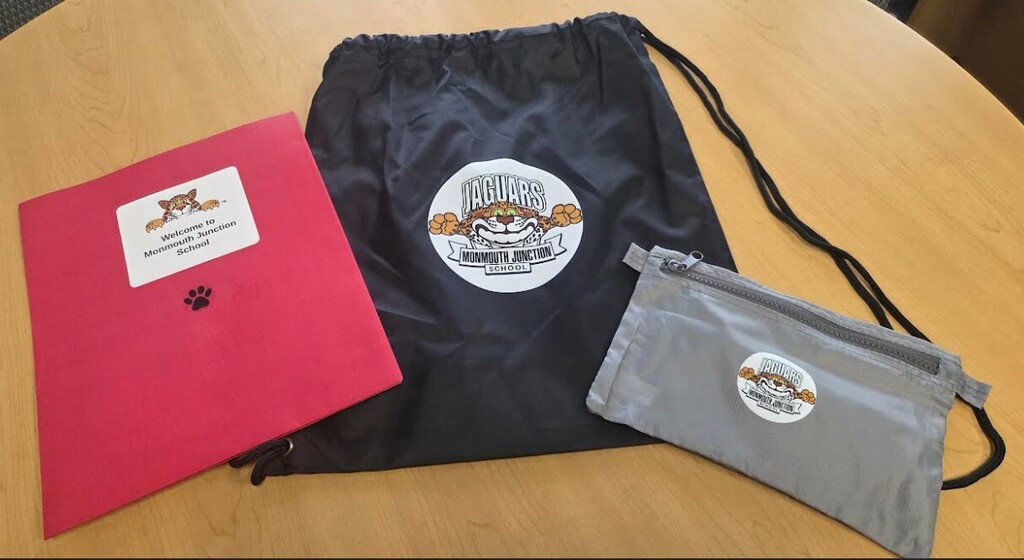 A black bag, red folder, and gray pouch on a wooden surface. The folder has a white label, and the bag features a white logo.
