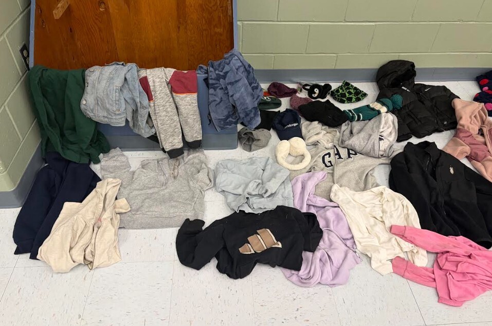 A pile of assorted clothing items, including jackets, pants, and hats, lies on a white floor.