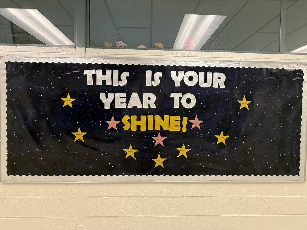 Black bulletin board with a space theme. White stars and text in yellow and pink fonts: "THIS IS YOUR YEAR TO SHINE!"